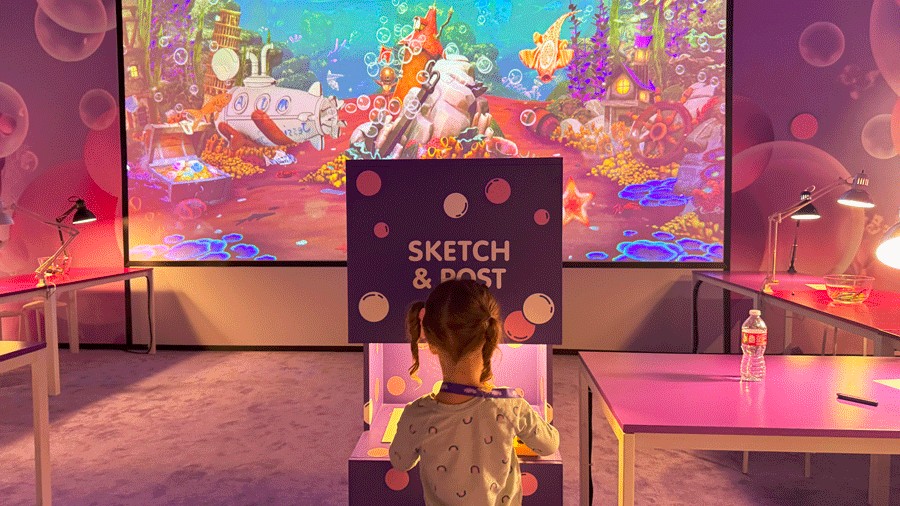 young girl with a coloring page projected onto a large screen with underwater world and customized designs