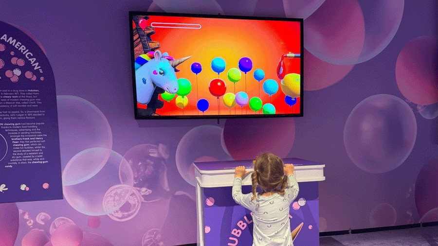 young girl playing interactive bubble-themed game, popping bubbles by stepping on a button