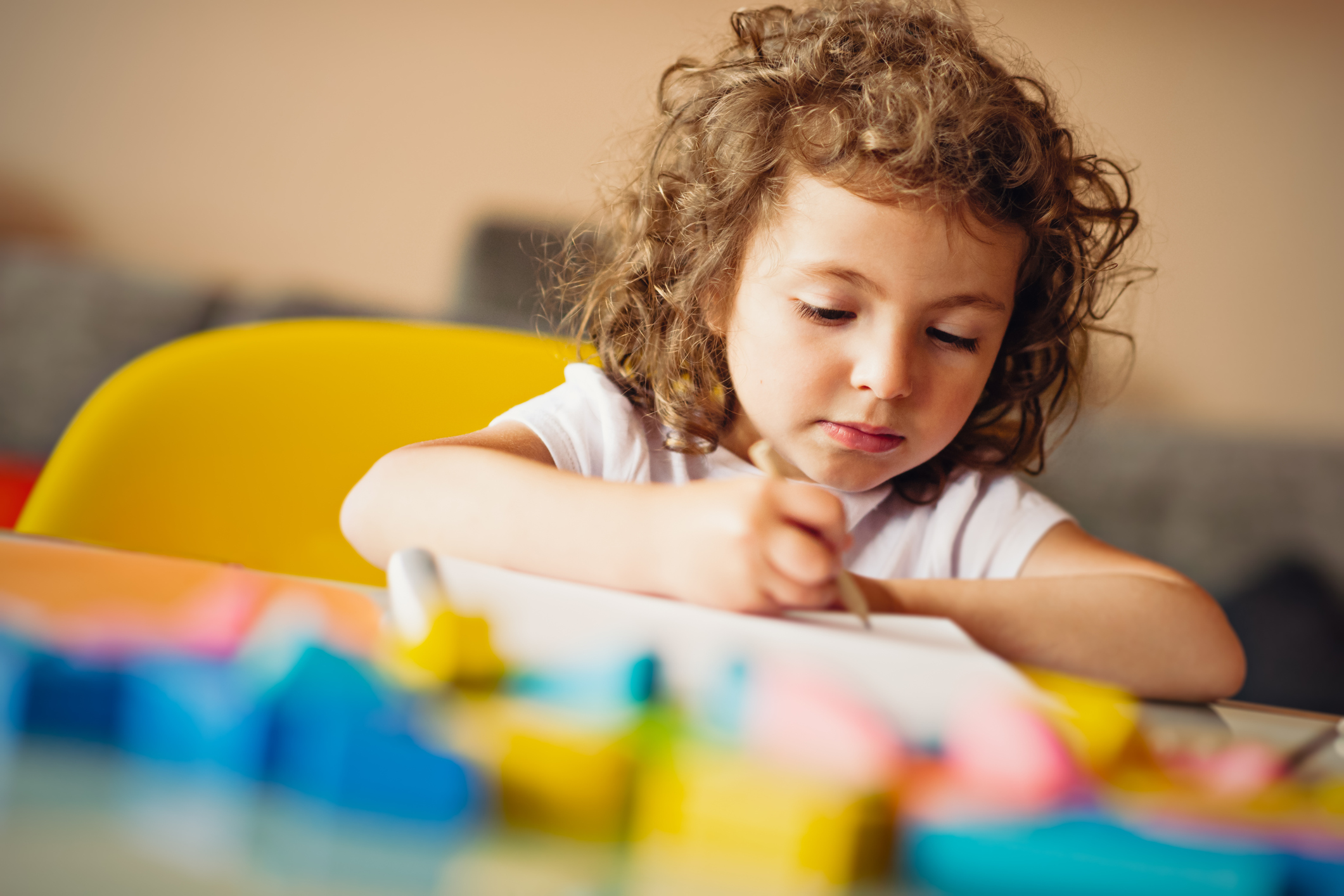 Young girl crafting at a table with a pencil in hand