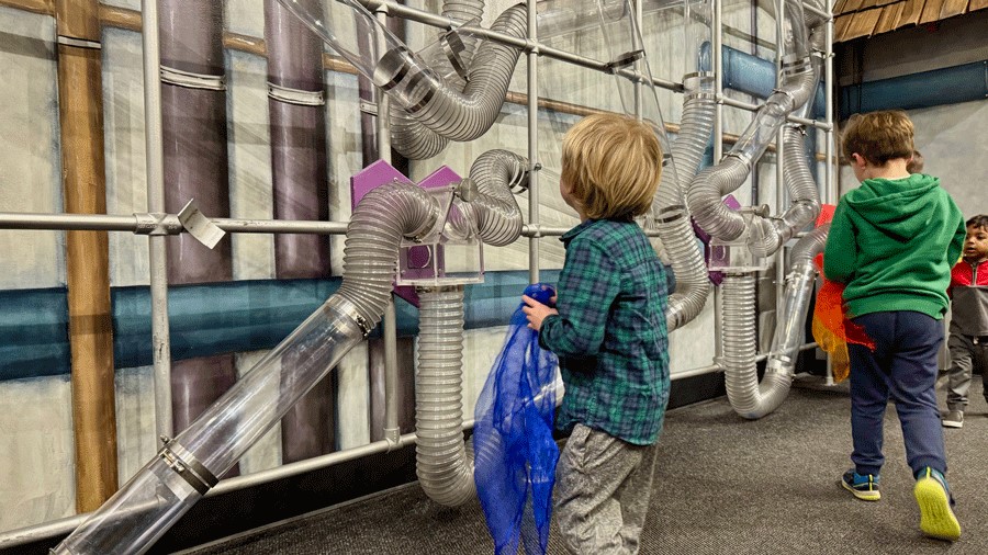 "Young boy watches scarves pass through air tube tunnels at Imagine Children’s Museum in Everett"