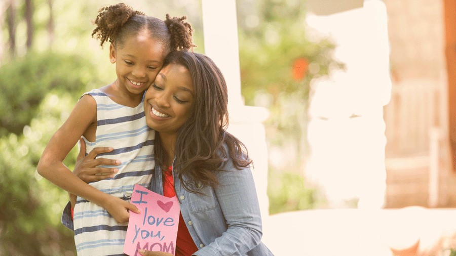 Mom hugging daughter with handmade Mother's Day card.