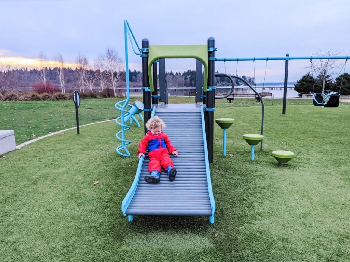 Small boy slides down the playground slide at Juanita Beach Park