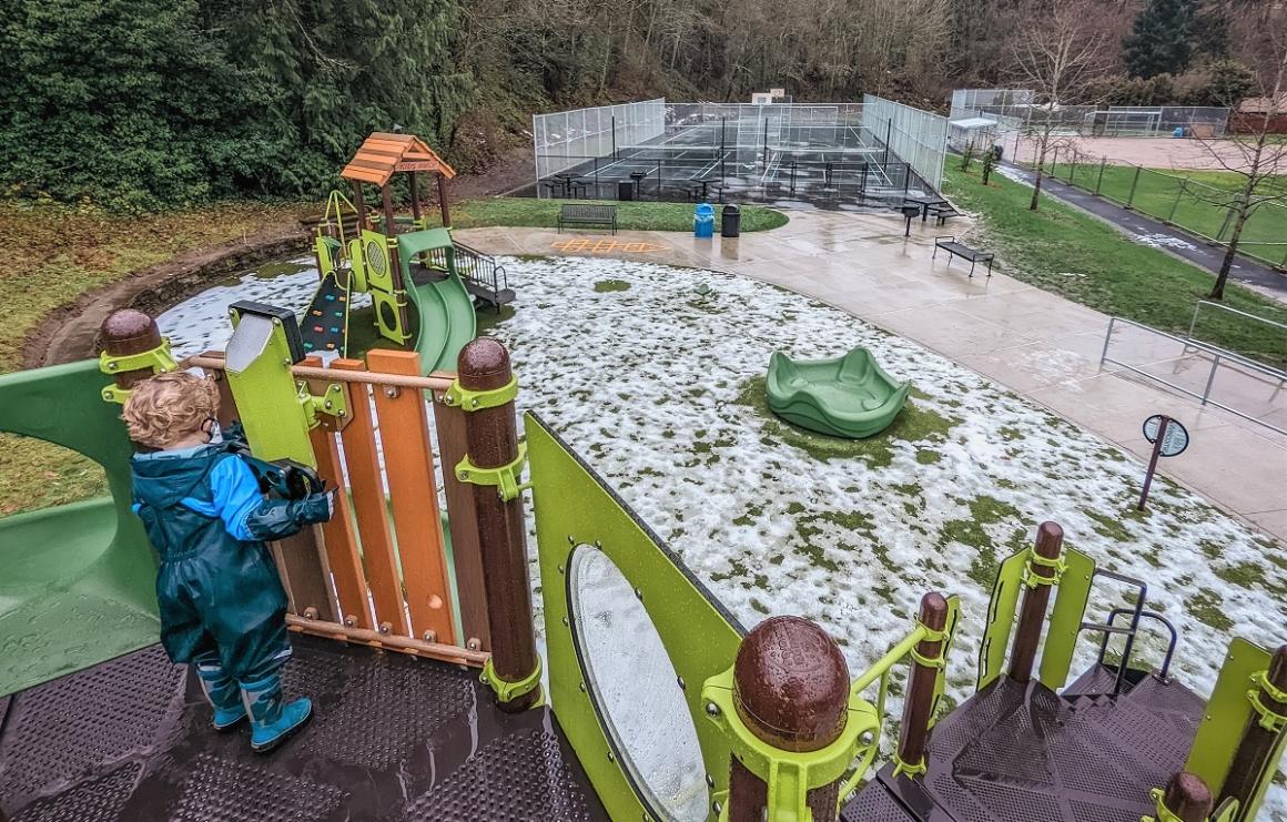 Aerial view of new Lakeridge Playground with boy playing and tennis courts visible in the background new playground seattle kids families