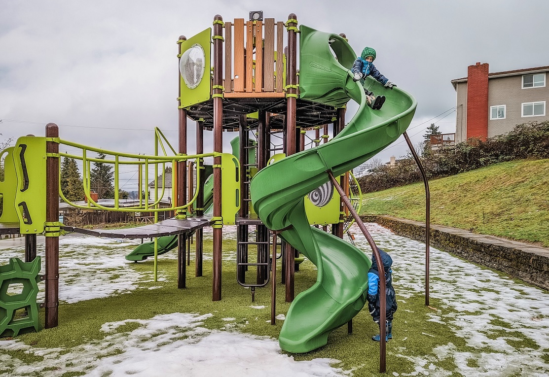 Kids play on the green twister slide at Lakeridge Playground new play area in South Seattle Rainier Beach neighborhood