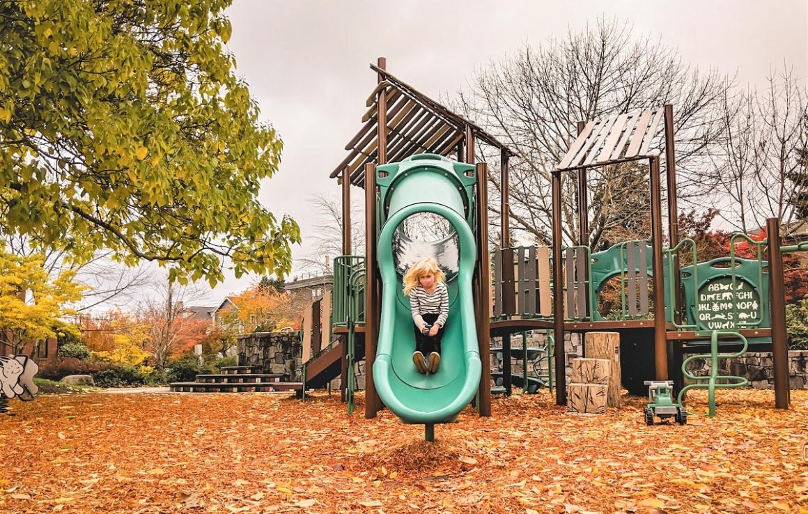 Girl descending a gree tube slide at the newly updated playground structure at Lakewood Playground in South Seattle