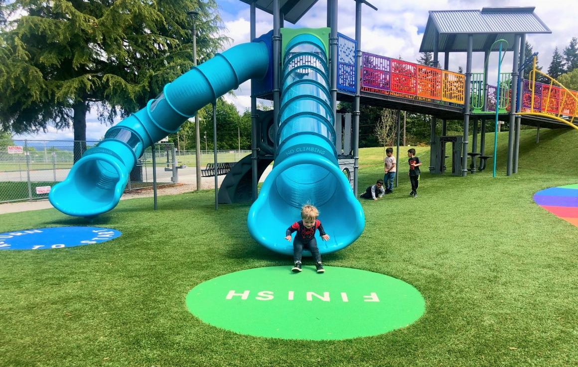 Child at the botton of a blue tube slide at West Fenwick Park's new playground near Seattle