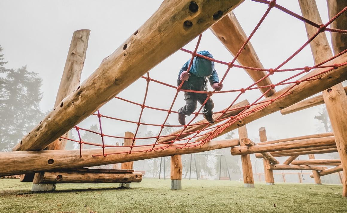 Boy on cargo net climber at new Westside Park playground as seen from underneath