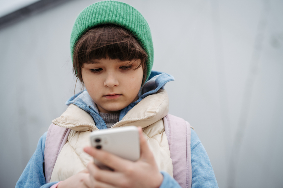 tween in green hat looks at a cell phone unhappily