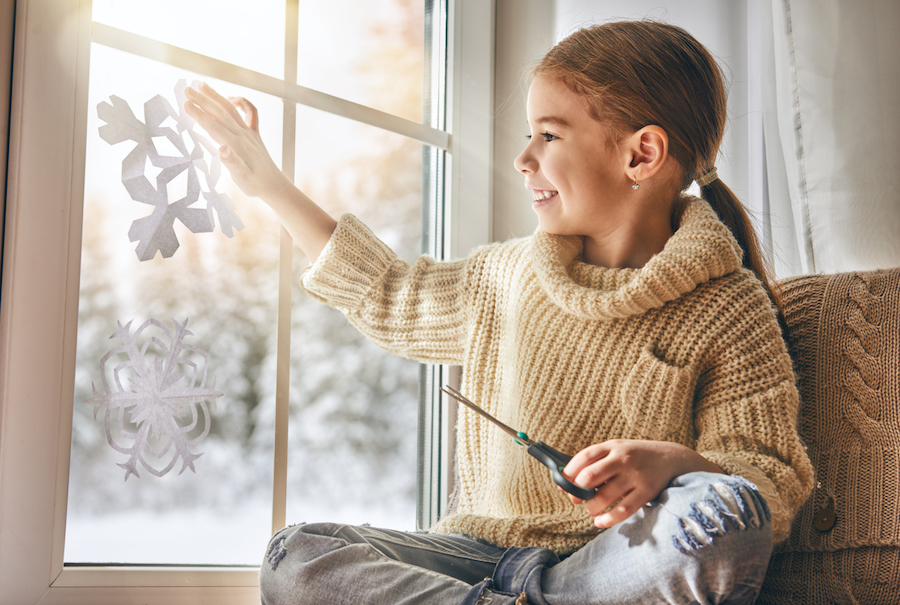 girl hangs a craft snowflake on the window for a holiday photo with beautiful light