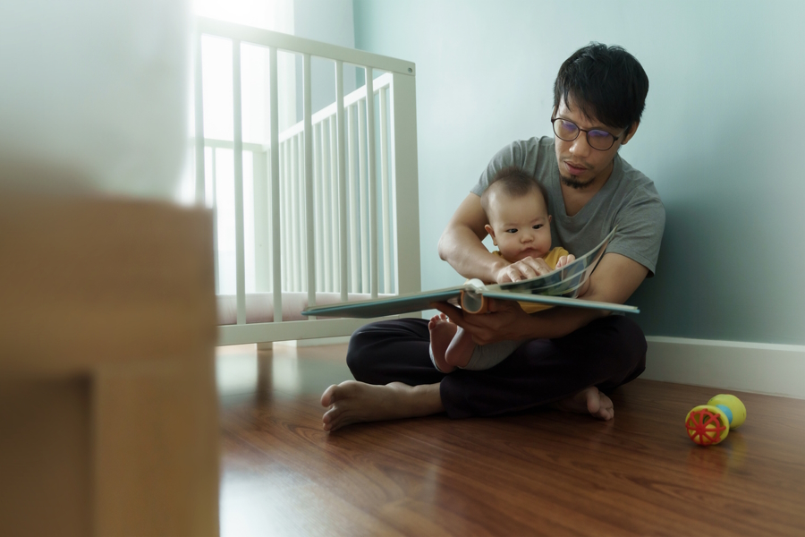 dad sitting on the floor reading a book to a baby