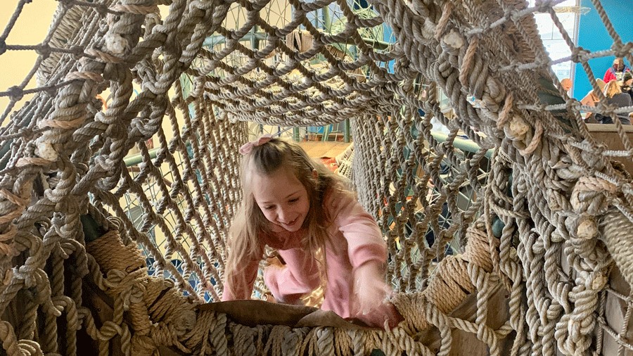 young girl climbing rope tunnel bridge at Children’s Museum of Tacoma, a local museum you can visit for free