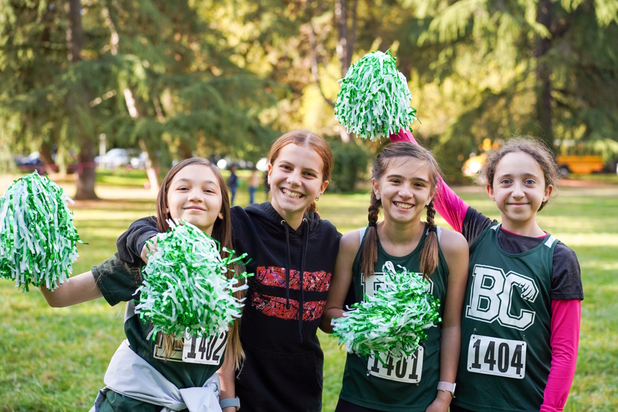 Girls standing together and smiling holding green and white pompoms 