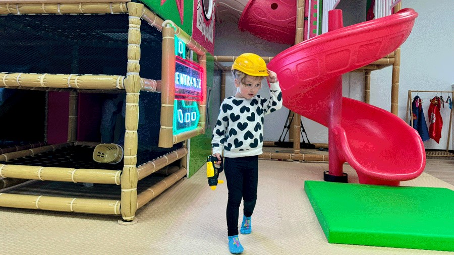 young girl wearing construction hat, playing pretend at Everett’s new indoor playground and cafe