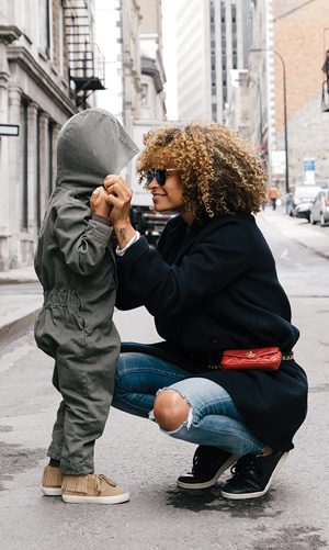 mother crouched down looking at her son on a city street with buildings in the background